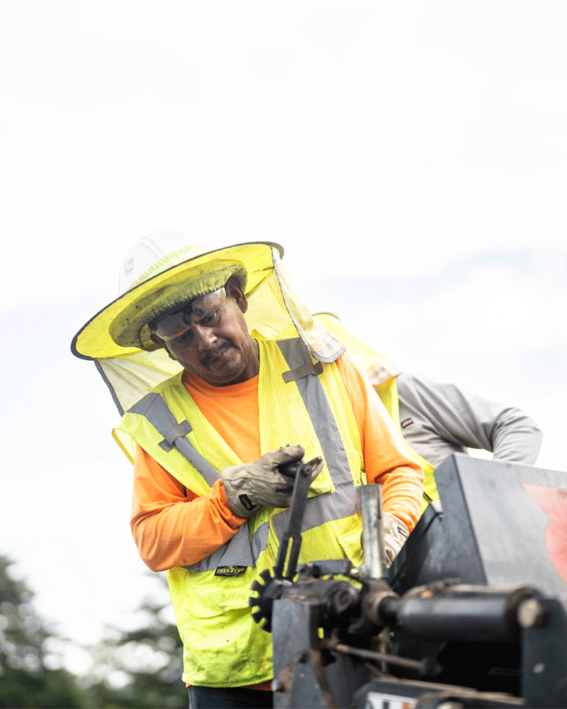 APCC, Close up of employee operating machine, yellow head cover, safety vest, 23137_BUILDWITT_0689