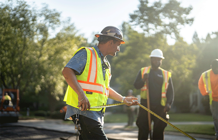 APCC, Employee in hard hat and vest holding measuring tape with employee in background, 23137_BUILDWITT_1803