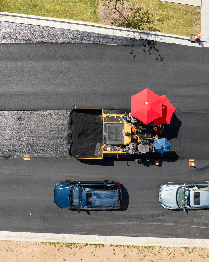 APCC, birds eye view of paving machine with red umbrella, cars going by below, 23137_BUILDWITT_2325